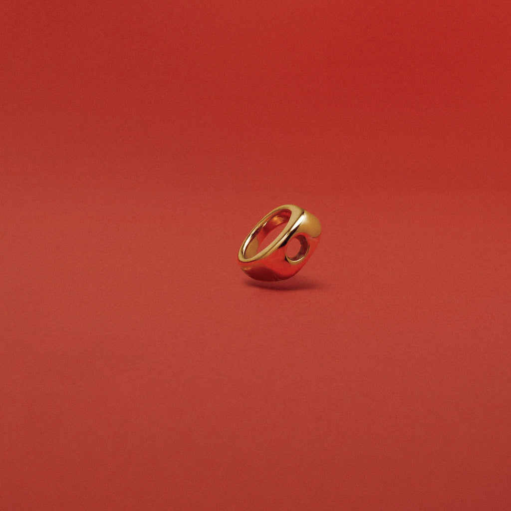 A small gold ring with a circular cutout, standing upright on a solid red background.