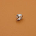 A silver ring with a small spherical bead on top, photographed on a solid warm brown background.