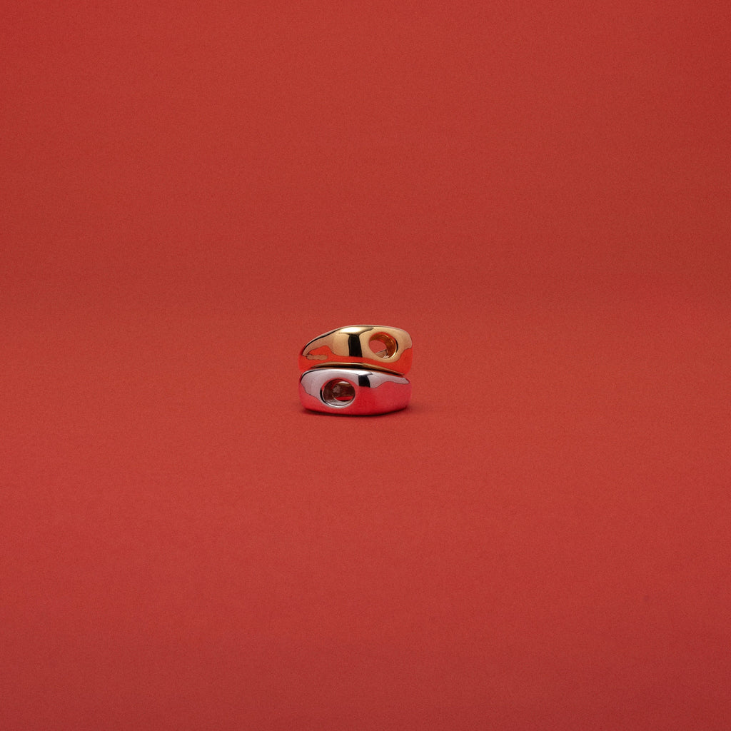 A small gold ring with a white enamel inlay and a red center detail, photographed against a solid red background.