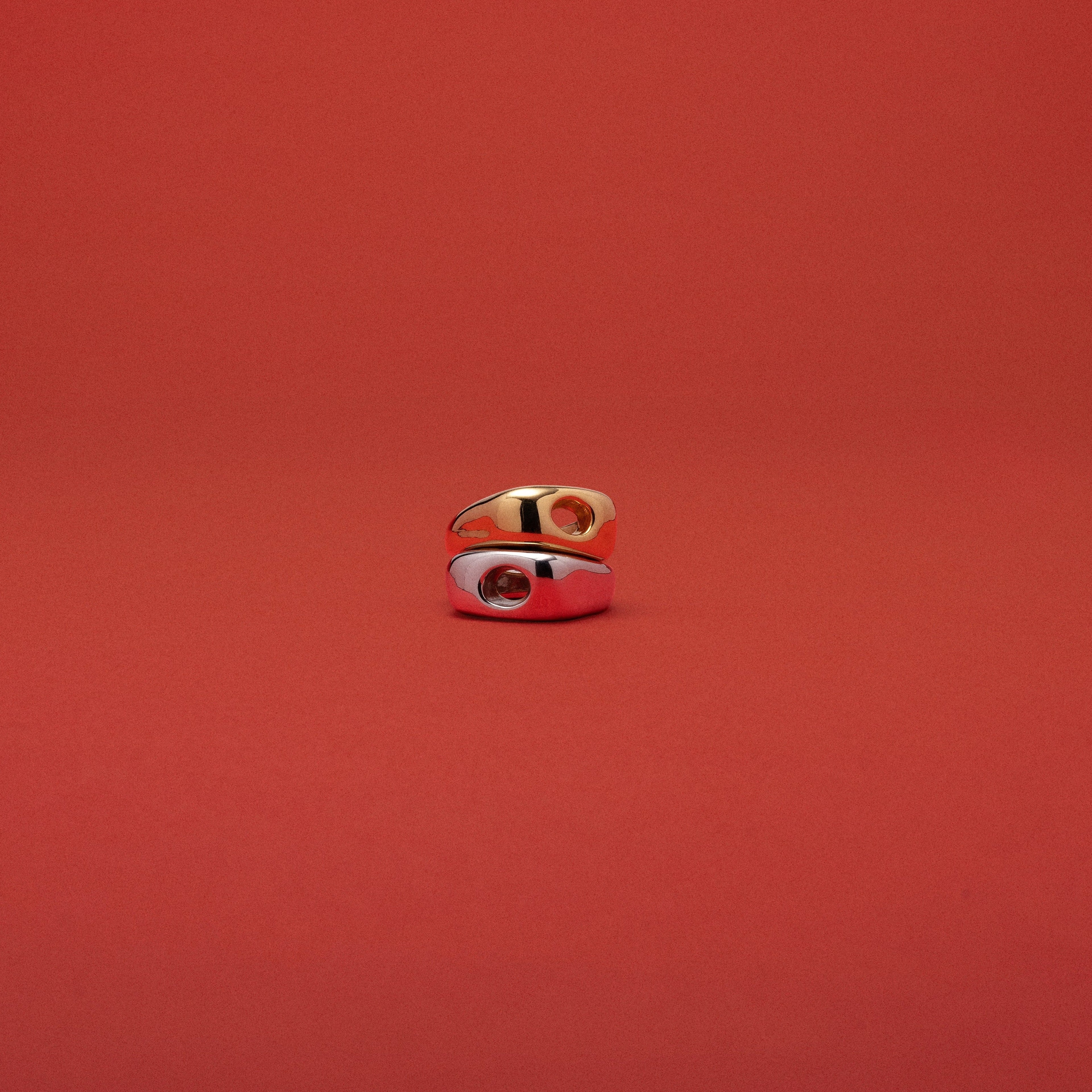 A small gold ring with a white enamel inlay and a red center detail, photographed against a solid red background.