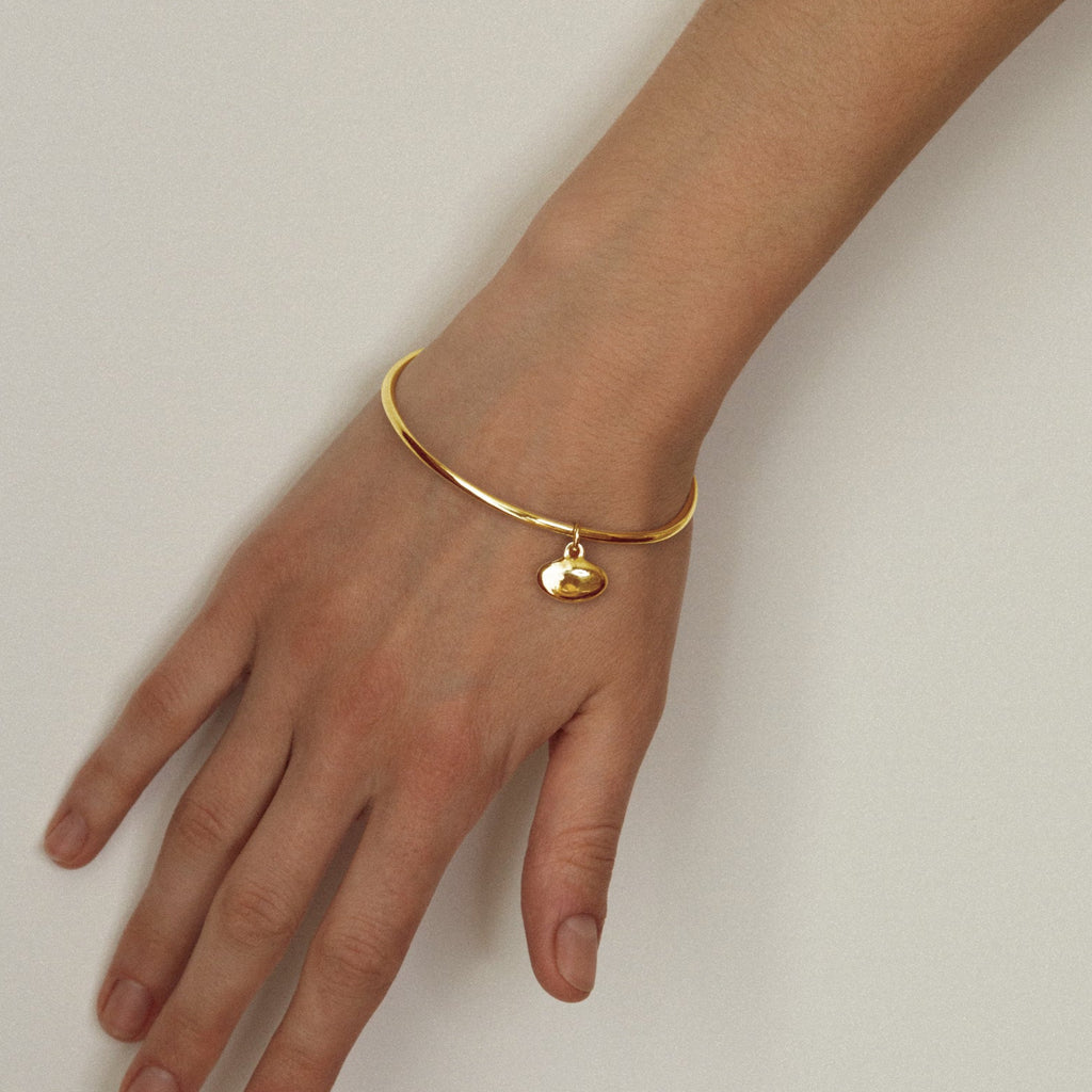 Gold bracelet with a heart charm on a wrist against a plain background