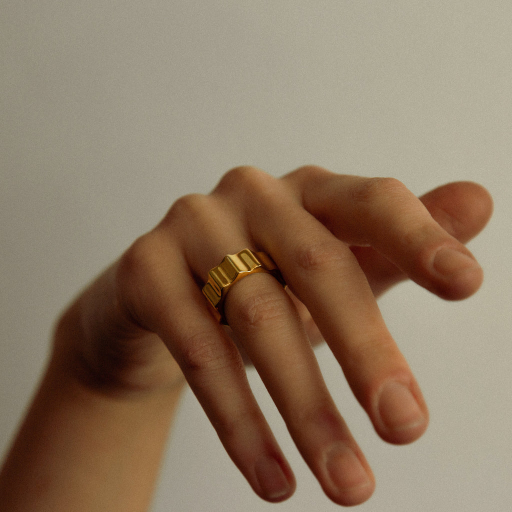 Hand wearing a gold ring on a plain background